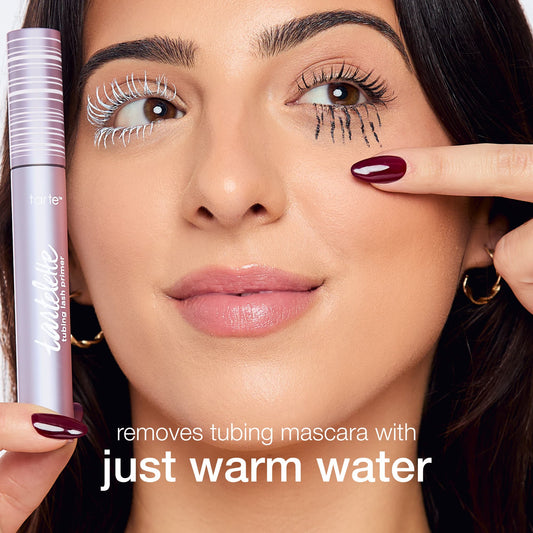 A person holds a Tarte Cosmetics mascara tube, showing lashes coated in white and black mascara. Text states, removes tubing mascara with just warm water. The background is plain white.